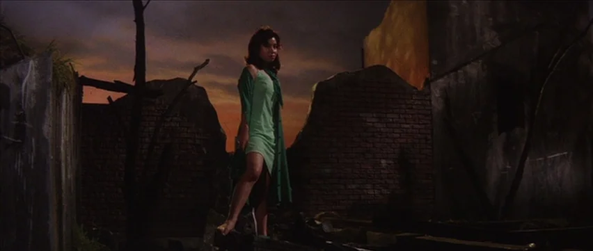 Gate of Flesh (1964) movie still: fullbody — A desolate urban lot features brick rubble and the silhouettes of dead trees. A young woman in a green…