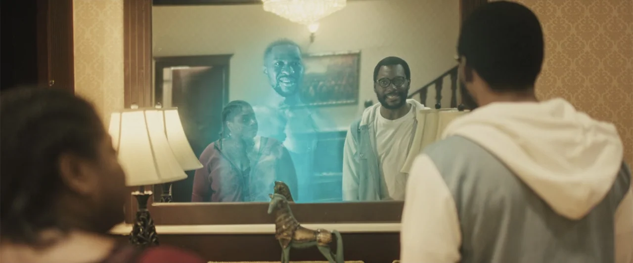 Casa De Novia (2024) movie still: medium — A domestic hallway features a large wooden-framed mirror hanging above a table lamp. A man stands before…