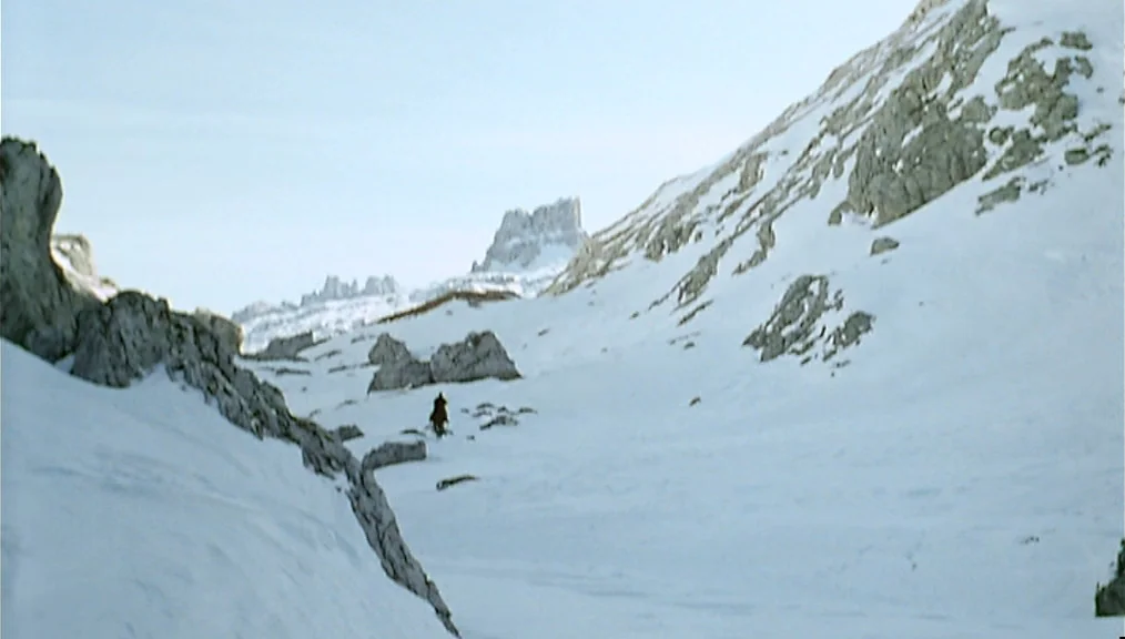The Great Silence (1968) movie still: wide — A vast, snow-covered mountain valley with craggy rocky peaks rising into a bright sky. A solitary…