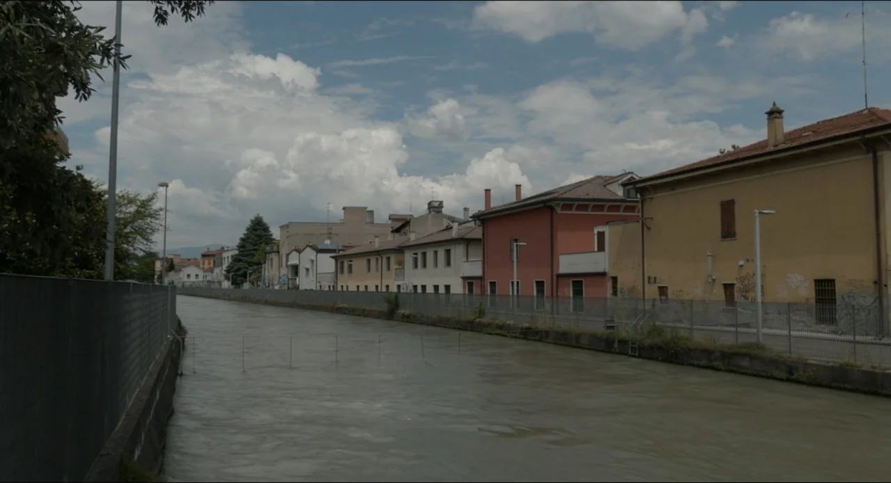 Federica Pellegrini - Underwater (2022) movie still: establishing — A murky river flows through an urban landscape with colorful old masonry…
