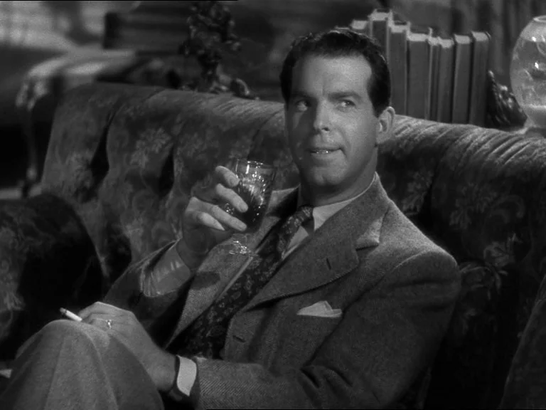 Double Indemnity (1944) movie still: medium — A man sits on a tufted sofa in a room filled with books. He holds a glass and a cigarette while…
