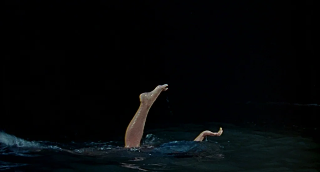Age of Consent (1969) movie still: wide — Dark, still water fills the frame against a black, featureless background at night. A woman's leg and hand…