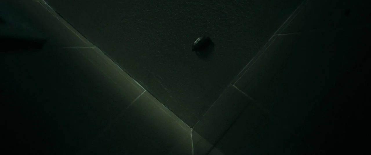 Saint Maud (2019) movie still: establishing — A dark corner where two ceiling planes meet at an sharp architectural angle. A single small circular…