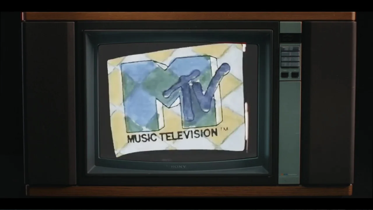 Lee Soo Man: King of K-Pop (2025) movie still: closeup — A vintage 1980s wood-paneled television set sits in a dark, empty space. The screen…