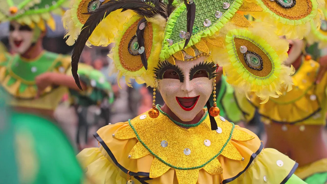 Awaken (2018) movie still: medium — A group of people wearing bright, sequined festival costumes perform in a street parade. The central figure…