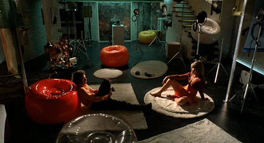 Perversion Story (1969) movie still: wide — A spacious studio apartment contains multiple inflatable round chairs and shag area rugs. A man and a…
