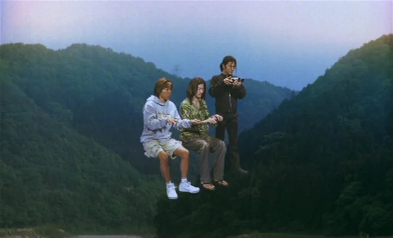 The Taste of Tea (2004) movie still: fullbody — Three men levitate in mid-air over a valley covered with dense green trees. The distant hills are…