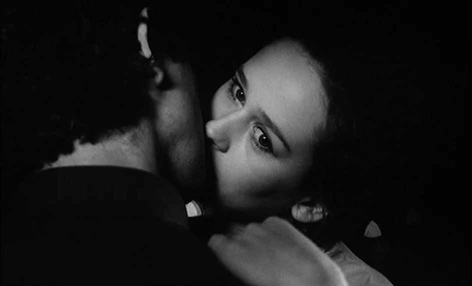 Boy Meets Girl (1984) movie still: closeup — A dark, featureless indoor space serves as the background for two people embracing. The woman leans…