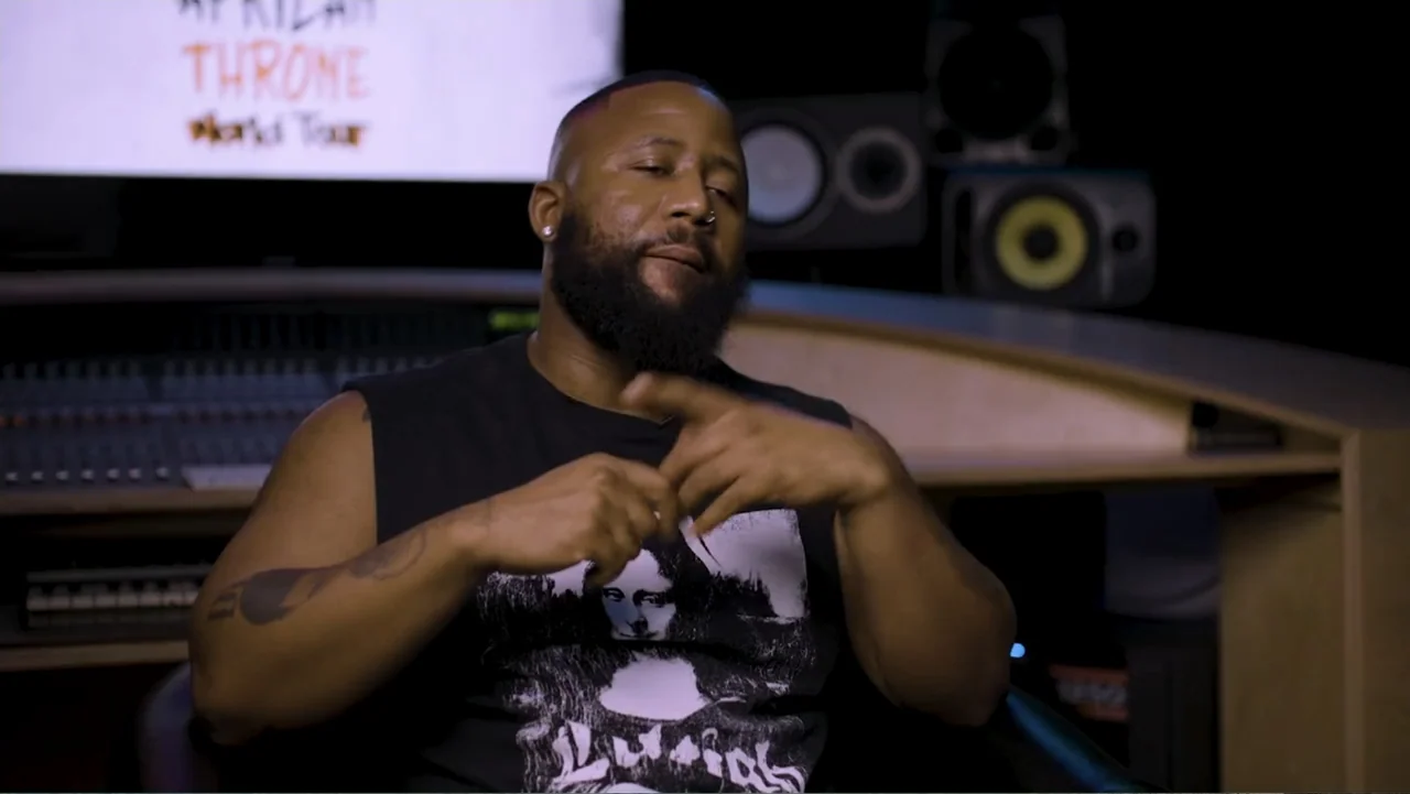 African Throne World Tour (2024) movie still: medium — A man sits in a professional audio recording studio with equipment visible in the background.…