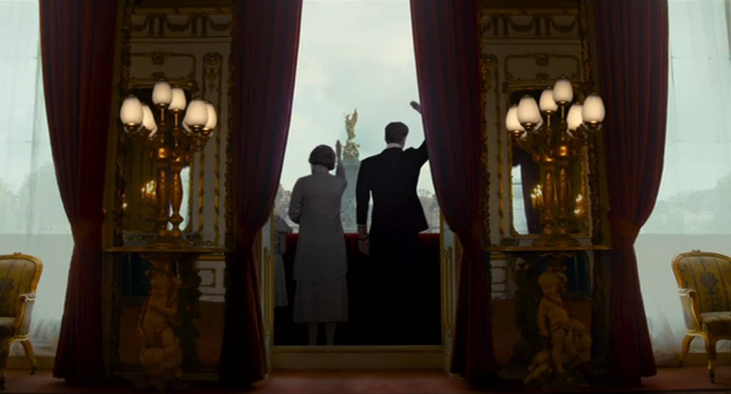 The King’s Speech (2010) movie still: wide — An opulent room with red velvet drapes and ornate gold lamps opens onto a balcony. A man and a woman…
