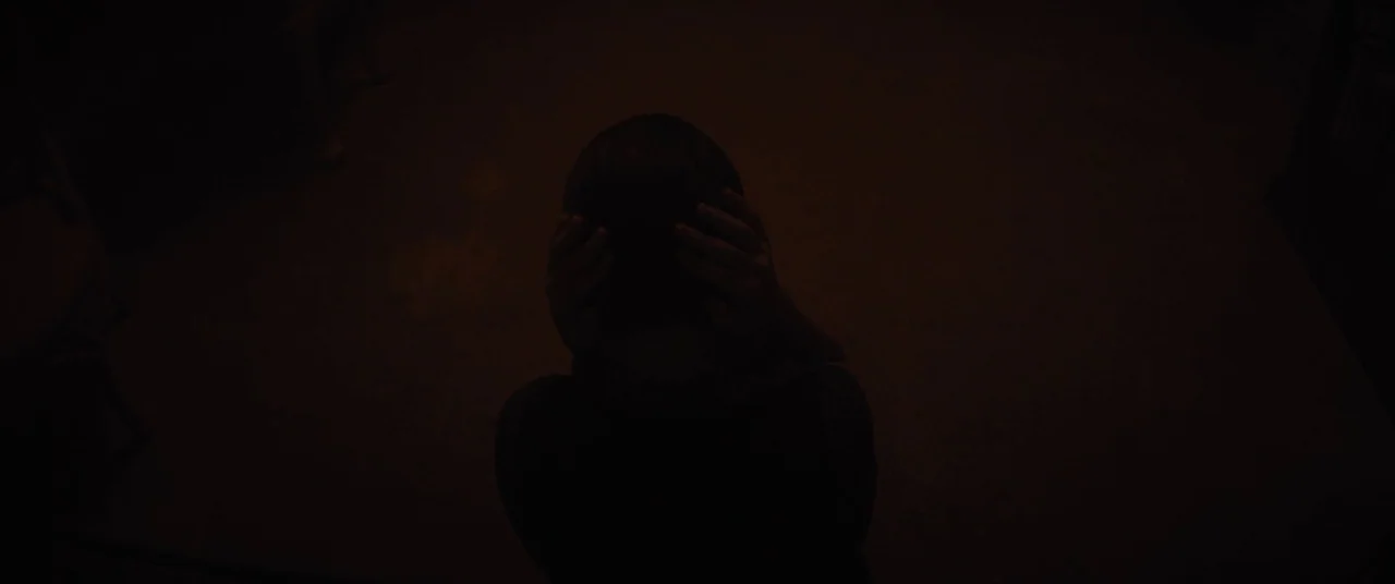 Daniel Isn’t Real movie still: medium — An interior space is rendered in deep, almost total darkness. A person is seen from directly above, hunched…