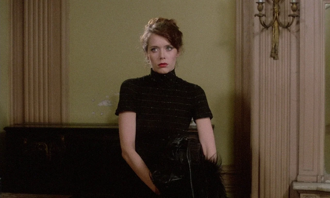 The Margin (1976) movie still: medium — A room with pale green walls featuring a wall sconce and molding. A woman in a dark turtleneck stands in the…