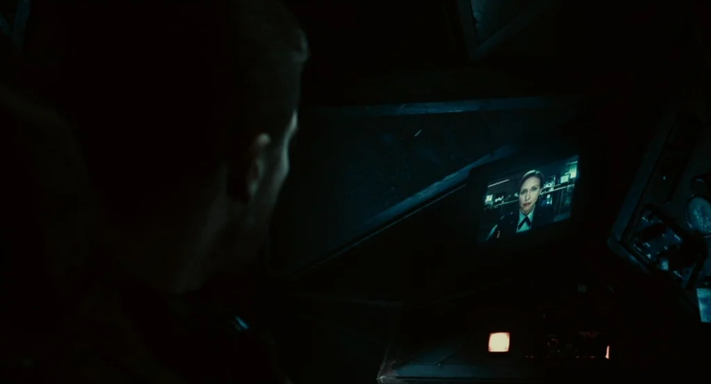 Source Code (2011) movie still: medium — A dark military cockpit interior featuring various control panels and a small glowing screen. A man viewed…