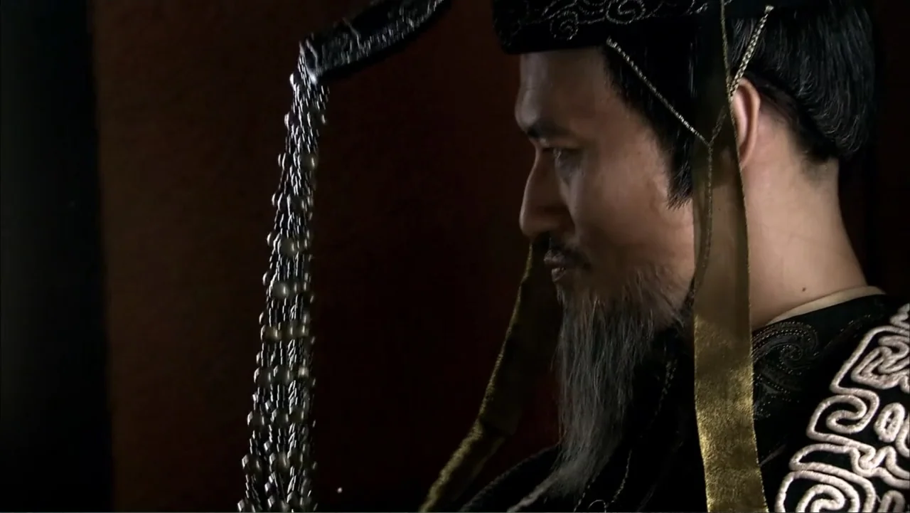 The First Emperor (2006) movie still: closeup — A dark interior with a dimly lit profile of a man wearing traditional robes. The man sits motionless…