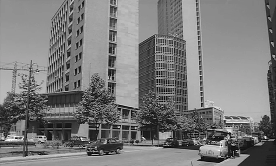 La Notte (1961) movie still: establishing — An urban intersection features tall mid-century modern office buildings and a construction crane.…