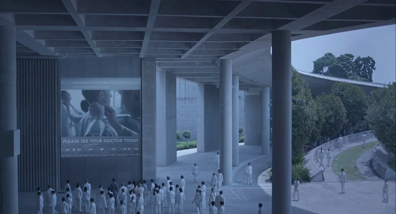Equals (2015) movie still: establishing — A modernist concrete plaza features massive support columns and a large digital announcement screen. Many…