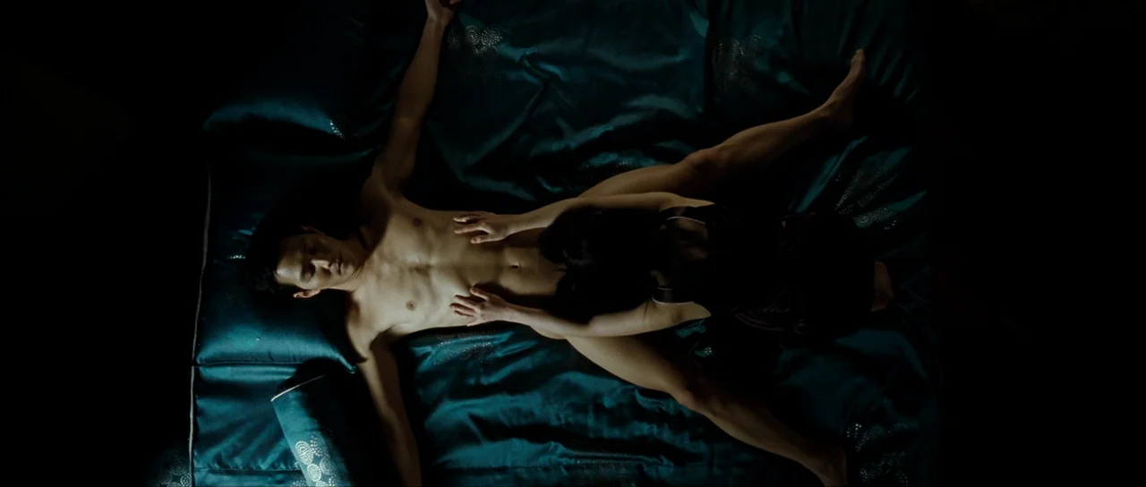 The Housemaid (2010) (2010) movie still: fullbody — A dark teal silk sheet covers the surface beneath two people in a bedroom. A woman straddles the…