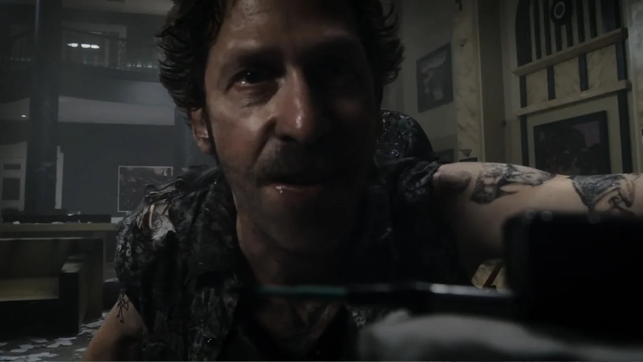 Flypaper (1999) movie still: closeup — A dimly lit room with blurred architectural details in the background and scattered papers. A man with a…