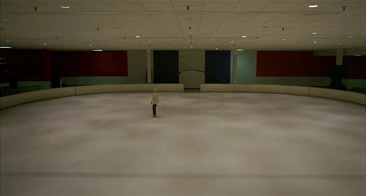Dawn of the Dead (1978) movie still: wide — A vast, empty indoor ice rink with red and dark blue wall panels. A solitary person stands in the middle…