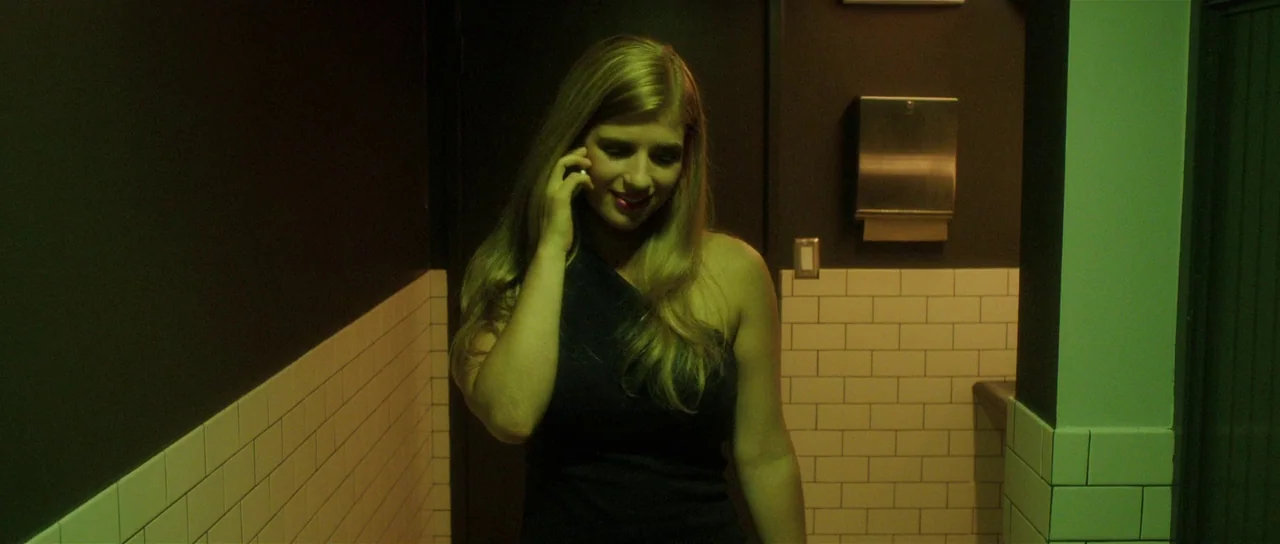 The Canyons (2013) movie still: medium — A modern restroom features dark paint above white rectangular wall tiles. A blonde woman in a black dress…