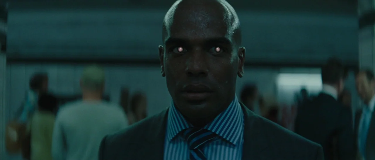 Suicide Squad (2016) movie still: medium — A dimly lit transit station with blurry commuters passing in the background. A man stands in the center…