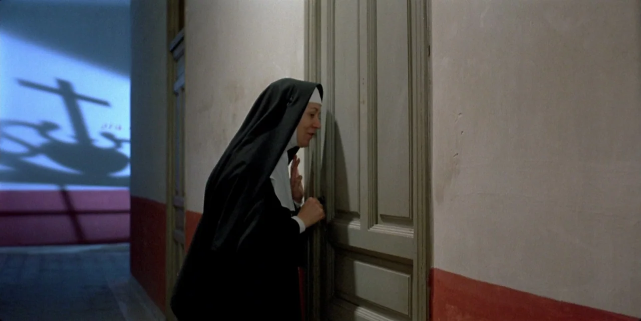 Dark Habits (1983) movie still: medium — A narrow corridor features plain white walls with a red painted wainscot. A nun in traditional black habit…