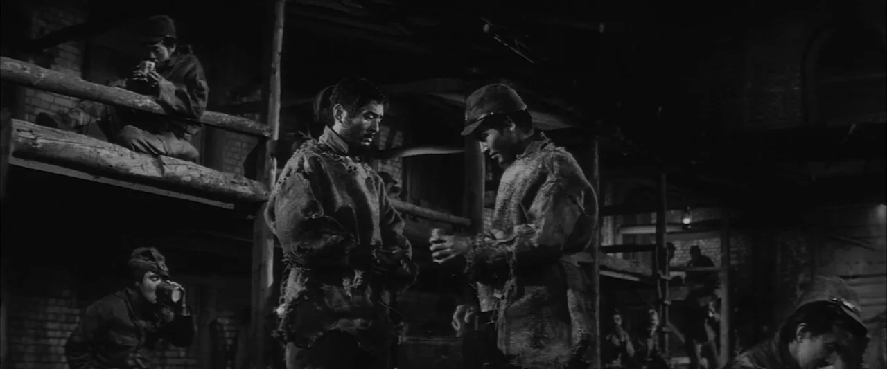 The Human Condition III: A Soldier’s Prayer (1961) movie still: medium — A dimly lit room with wooden bunk beds stacked against rough brick walls.…