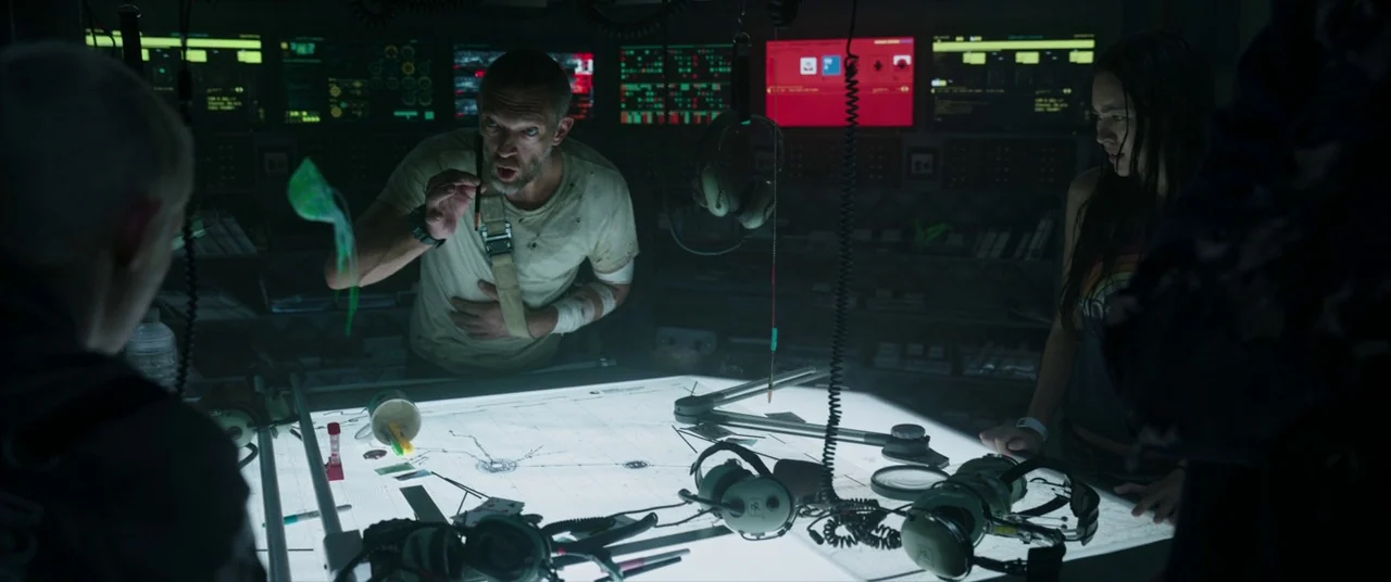 Underwater (2020) movie still: medium — A dark command room filled with illuminated monitors and a large, glowing central map. A bearded man points…