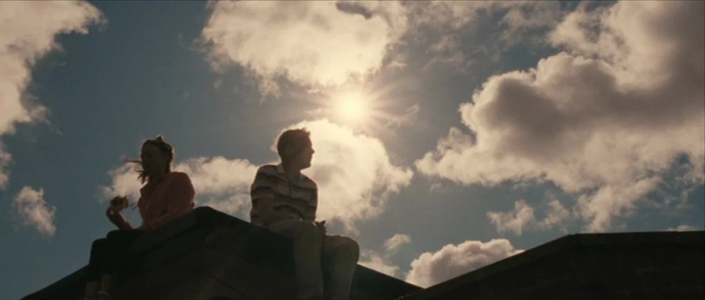 The Scouting Book for Boys (2009) movie still: wide — Two teenagers sit on a tiled residential roof against a bright daytime sky. The sun shines…