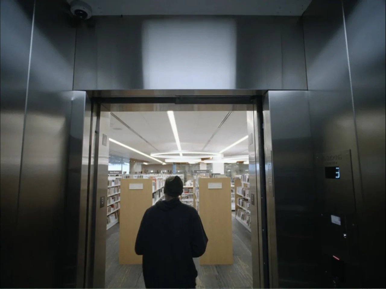 As We Speak: Rap Music on Trial (2024) movie still: medium — A stainless steel elevator interior opens to reveal a brightly lit library interior. A…