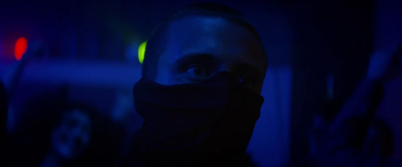 Kissing Candice (2017) movie still: closeup — A dark, dimly lit environment features colored neon lights blurring in the background. A man with a…