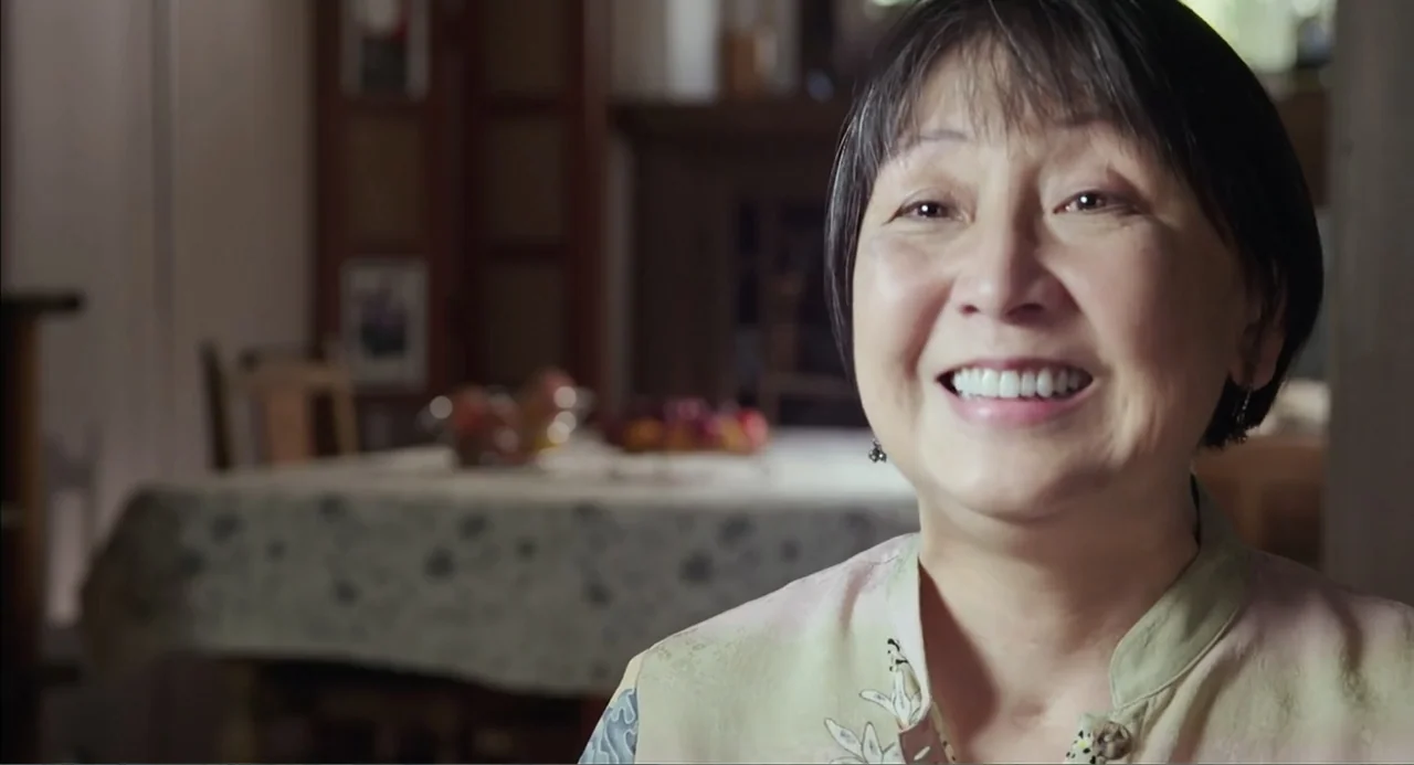 Free Chol Soo Lee (2022) movie still: closeup — An interior dining space with a table covered by a patterned cloth in back. A woman with short hair…