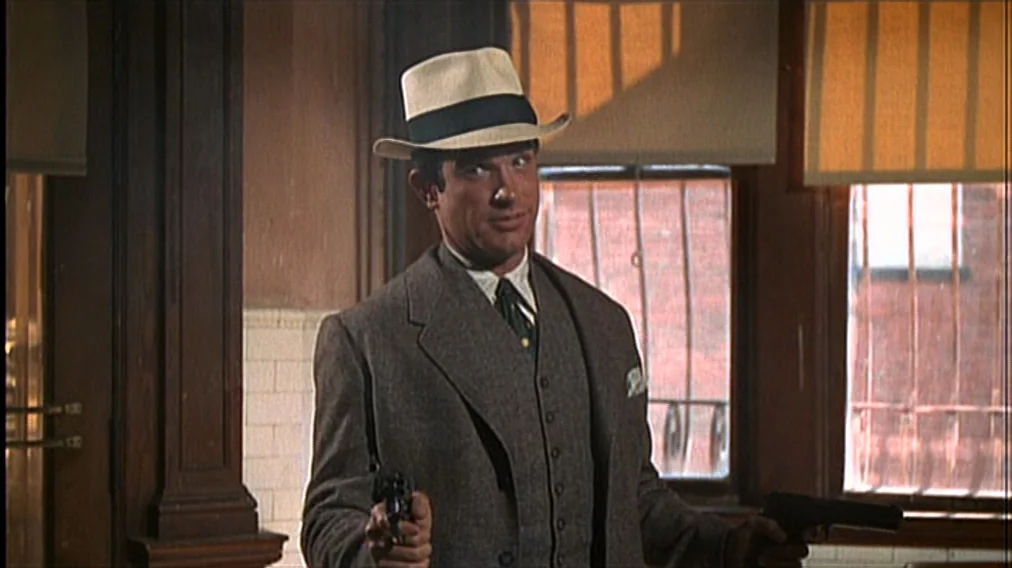 Bonnie And Clyde (1967) movie still: medium — A man stands in a dimly lit office with wooden paneling and barred windows. He holds a pistol in each…