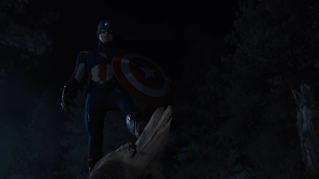 The Avengers (2012) movie still: fullbody — A dark, nighttime forest environment filled with dense tree silhouettes. A costumed figure stands…