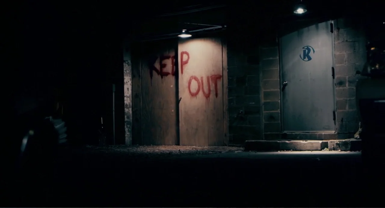 Terrifier (2018) movie still: wide — A dark outdoor space features a wooden gate with painted text and a door. Red paint spells out the words keep…