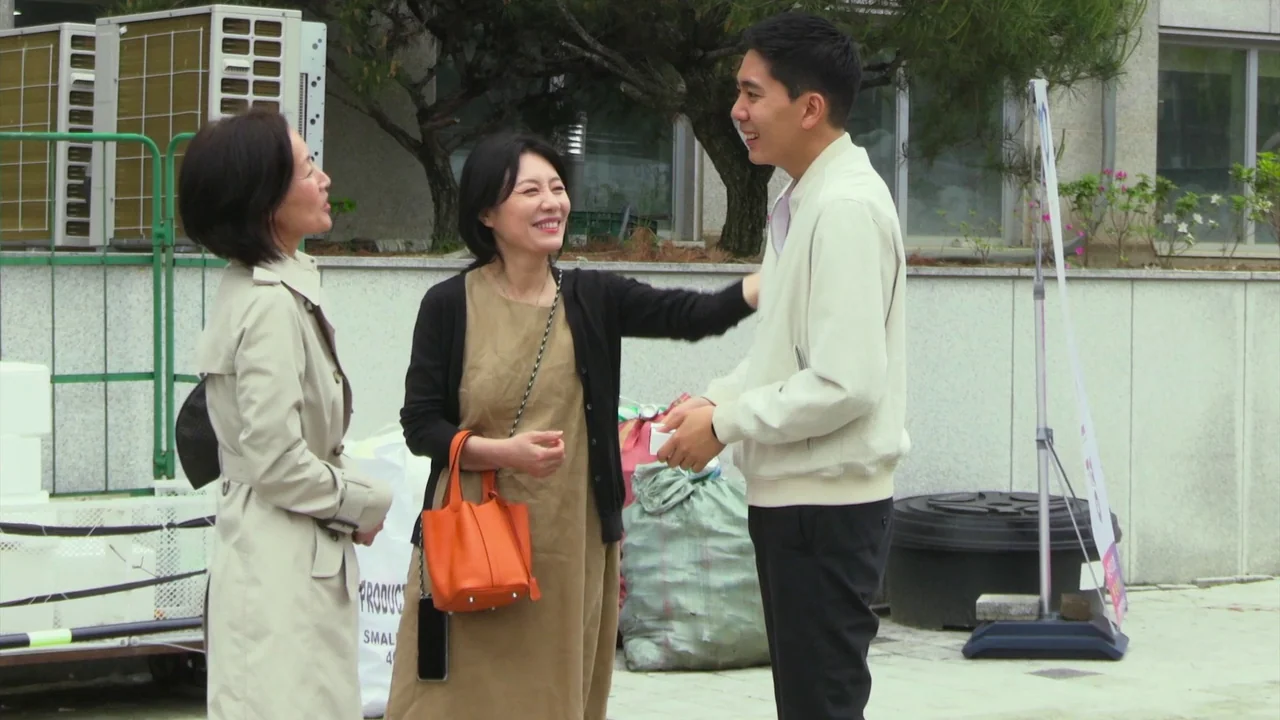 In Front Of Your Face (2021) movie still: fullbody — A paved area outside a building features air conditioning units and large sacks. A woman in a…