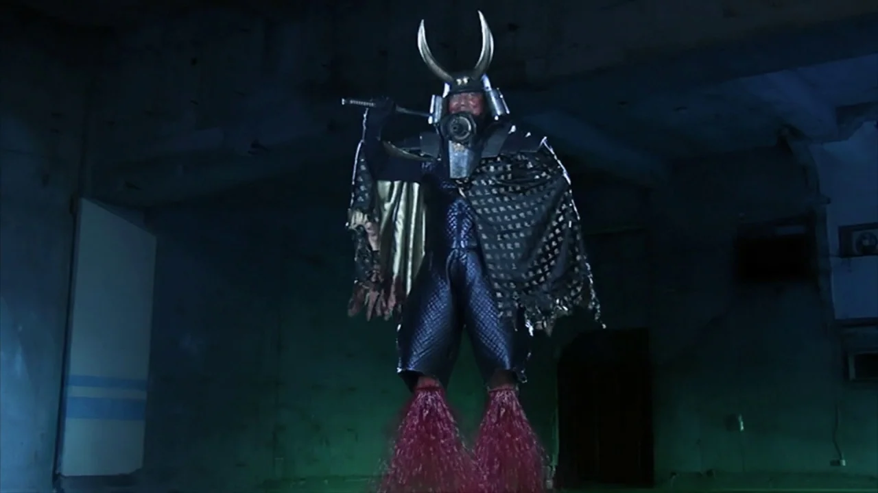 Tokyo Gore Police (2008) movie still: fullbody — A dark, dilapidated concrete structure with peeling walls serves as the backdrop. An armored…