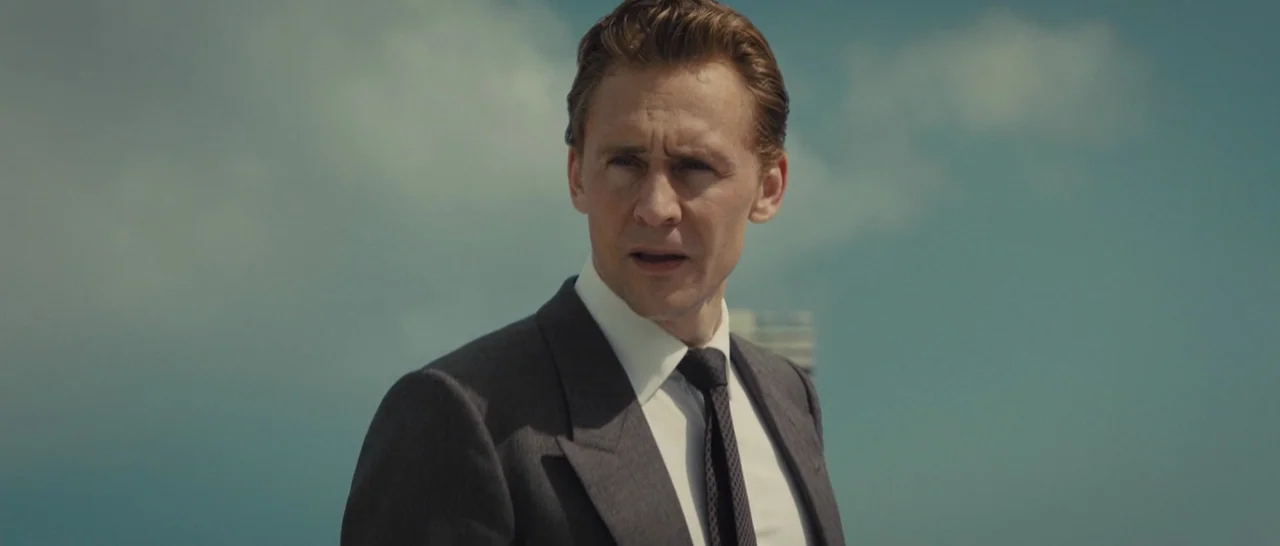 High-Rise (2015) movie still: medium — A man stands outdoors on a rooftop with a blurred sky and indistinct architecture. He gazes away from the…