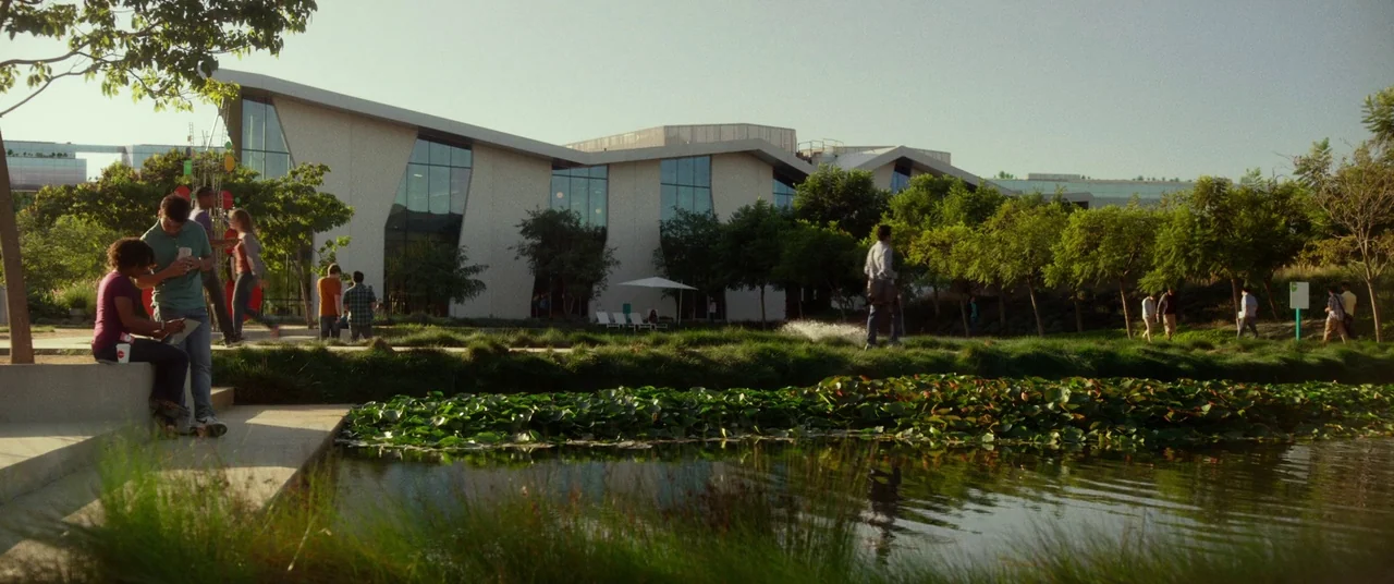 The Circle (2017) movie still: wide — A modern office or university campus building features expansive glass windows and angular architecture.…