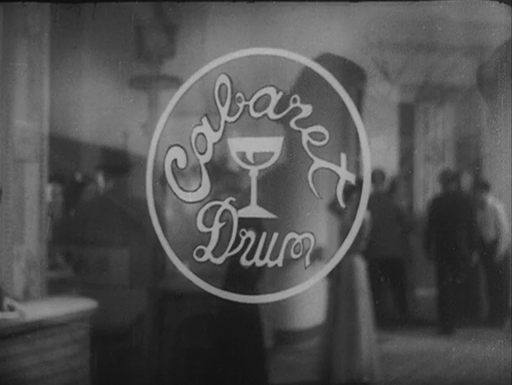 Anatomy of a Relationship (1976) movie still: closeup — A glass door features the logo of the Cabaret Drum in white lettering. People in silhouette…