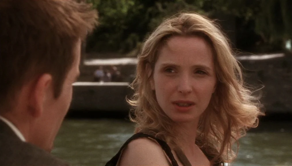 Before Sunset (2004) movie still: medium — A woman stands by a riverbank with water and stone walls in the background. She turns her head to look at…