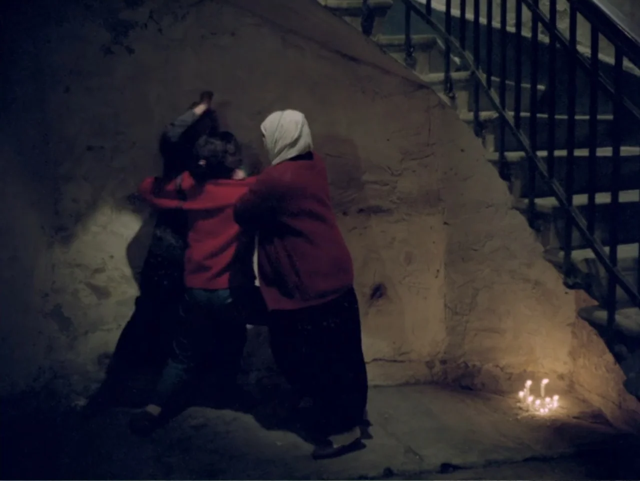 Don't Let Them Shoot the Kite (1989) movie still: medium — A dimly lit stone staircase landing with dark walls and a metal railing. Two people…