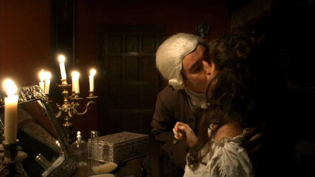 A Cock and Bull Story (2005) movie still: medium — A dimly lit room contains a wooden vanity with candles and silver accessories. A man wearing a…