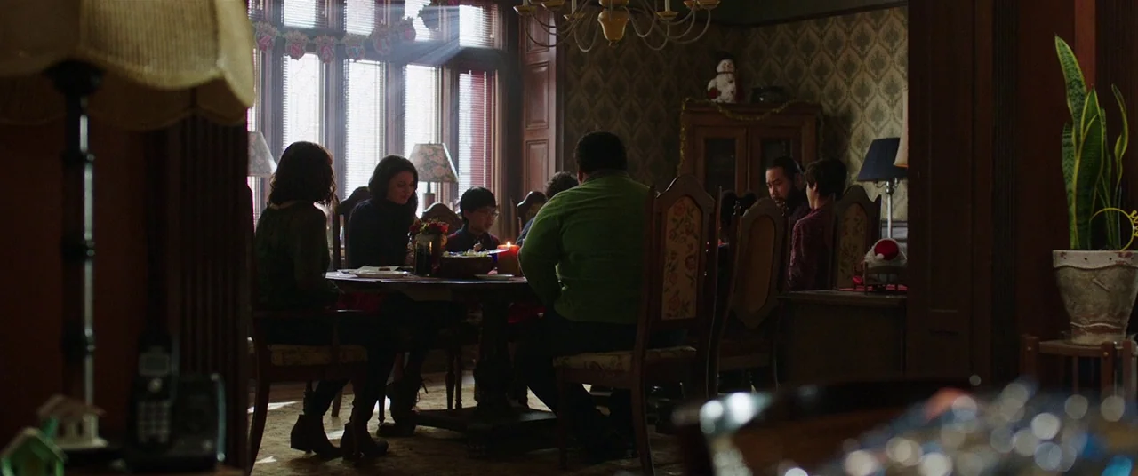 Shazam! (2019) movie still: wide — A traditional dining room with patterned wallpaper, wood paneling, and a circular table. A group of people sits…