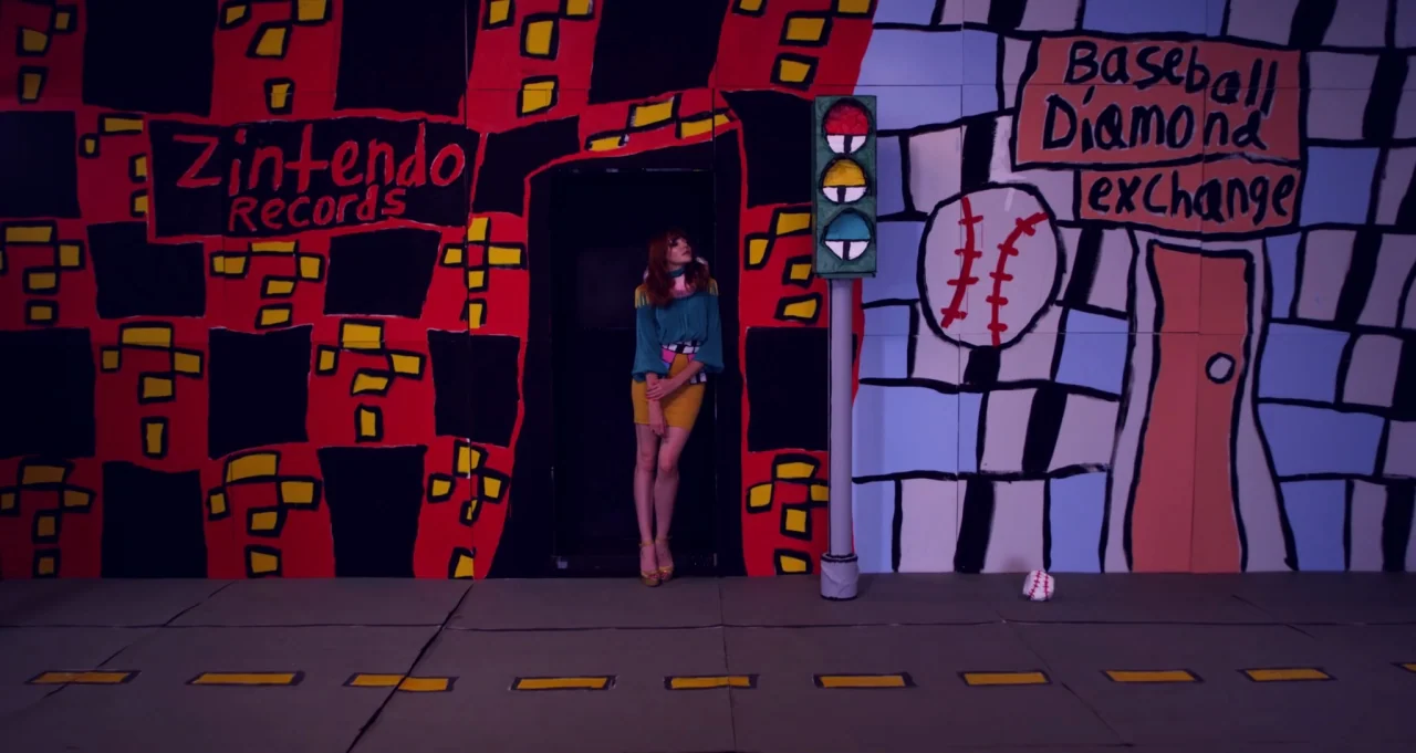 Adam Green’s Aladdin (2016) movie still: wide — A theatrical flat-painted set mimics a cartoonish street with signs for records and baseball. A…