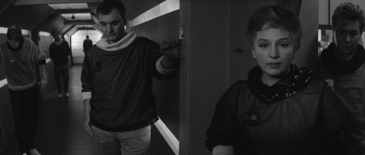 Ikarie XB 1 (1963) movie still: medium — A sterile futuristic corridor features geometric wall panels and overhead lighting strips. A man stands…
