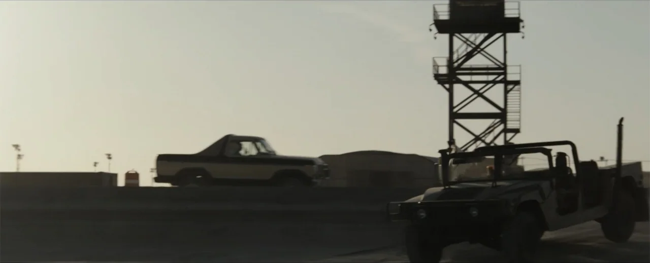 Venom: The Last Dance (2024) movie still: wide — A flat desert environment features a tall metal watchtower standing against a bright sky. A…