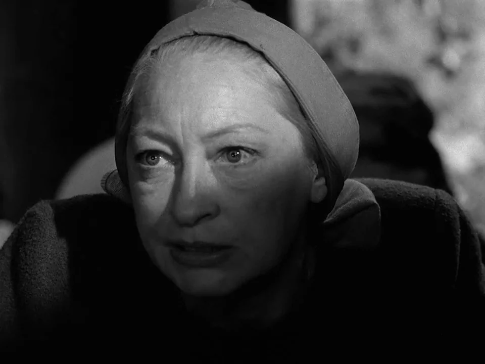 The Seventh Seal (1957) movie still: closeup — A dimly lit room provides the backdrop for a close-up of an elderly woman. The woman stares ahead…