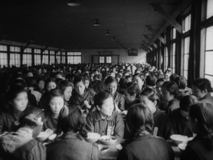 The Most Beautiful (1944) movie still: wide — A long, industrial mess hall filled with many people sitting at long wooden tables. The room has high…