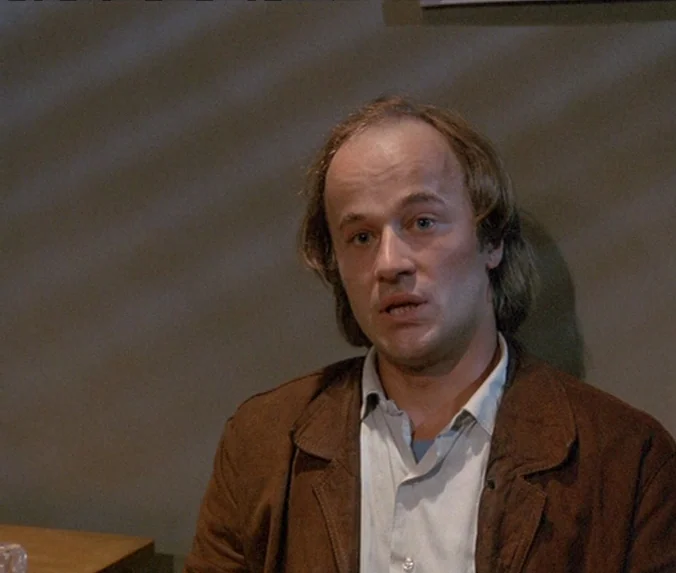 Crime & Punishment (1983) movie still: medium — A man stands in a room with light-colored walls marked by soft shadow patterns. He faces the camera…
